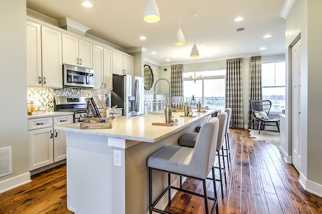 kitchen featuring stainless steel appliances, hanging light fixtures, an island with sink, and white cabinets