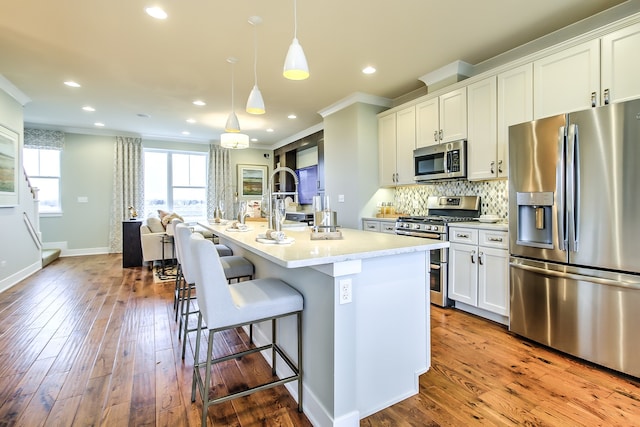 kitchen with hanging light fixtures, appliances with stainless steel finishes, an island with sink, and white cabinetry