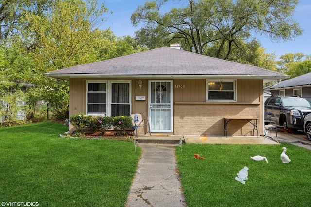 view of front of property with roof with shingles, brick siding, a chimney, and a front yard