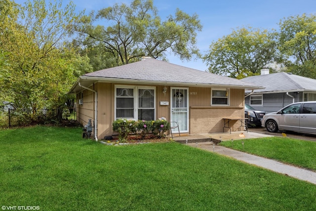 view of front of house featuring roof with shingles, fence, a front lawn, and brick siding