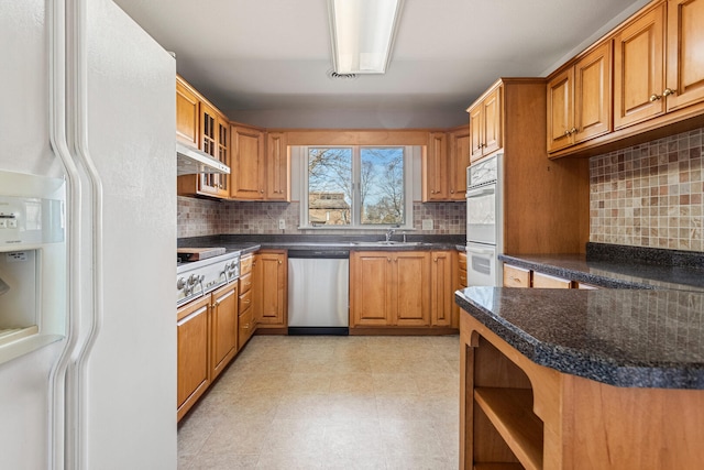 kitchen with stainless steel appliances, tasteful backsplash, dark countertops, and brown cabinets