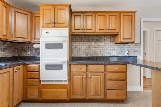 kitchen featuring dark countertops, brown cabinets, decorative backsplash, and white double oven