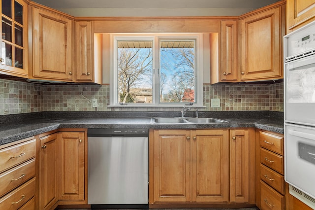 kitchen with tasteful backsplash, dark countertops, dishwasher, and a sink