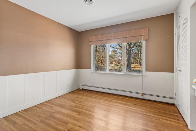 spare room with a wainscoted wall, a baseboard radiator, visible vents, and light wood-style floors