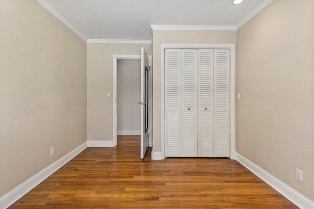 unfurnished bedroom featuring crown molding, a closet, baseboards, and wood finished floors