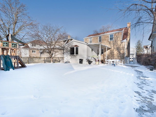 snow covered rear of property with a residential view, a playground, fence, and a chimney