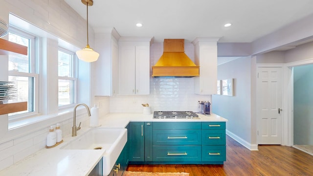 kitchen with pendant lighting, custom range hood, stainless steel gas stovetop, white cabinetry, and a sink