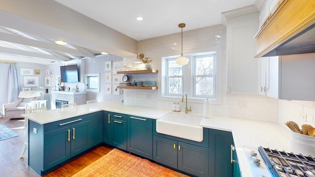 kitchen with pendant lighting, light countertops, open floor plan, a sink, and a peninsula