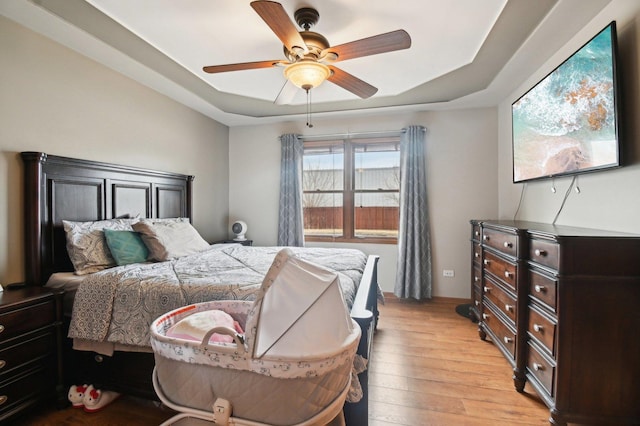 bedroom featuring a raised ceiling, ceiling fan, and light wood finished floors