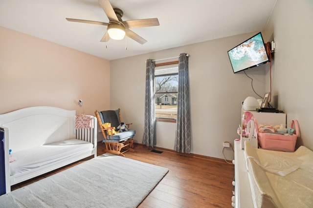 bedroom with a ceiling fan, a nursery area, and wood-type flooring