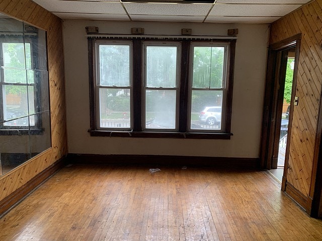 spare room with a paneled ceiling, baseboards, wood walls, and light wood finished floors