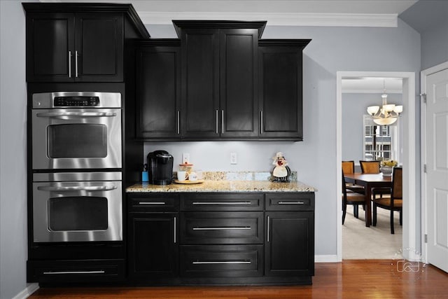 kitchen featuring dark cabinets, stainless steel double oven, crown molding, and light stone counters