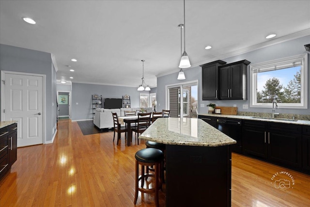 kitchen featuring a breakfast bar area, a sink, dark cabinetry, light wood finished floors, and crown molding