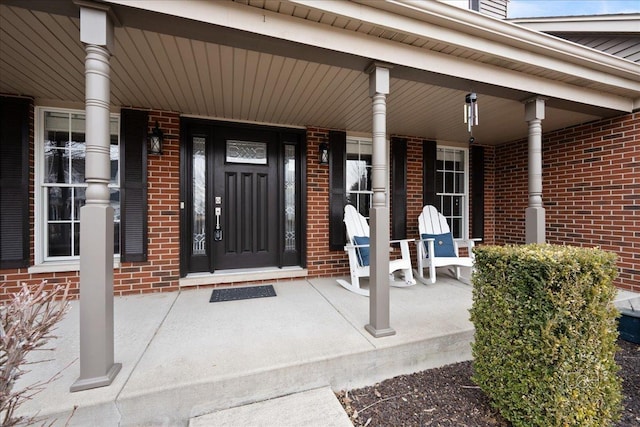 view of exterior entry with a porch and brick siding