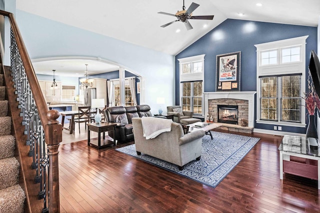 living area featuring arched walkways, wood-type flooring, a stone fireplace, and stairs