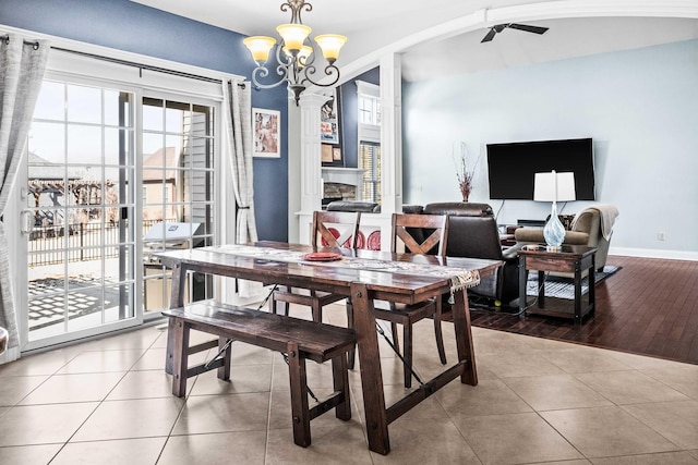 dining area with baseboards, a fireplace, ceiling fan with notable chandelier, and tile patterned floors