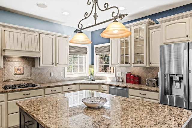 kitchen featuring a kitchen island, glass insert cabinets, light stone countertops, stainless steel appliances, and pendant lighting