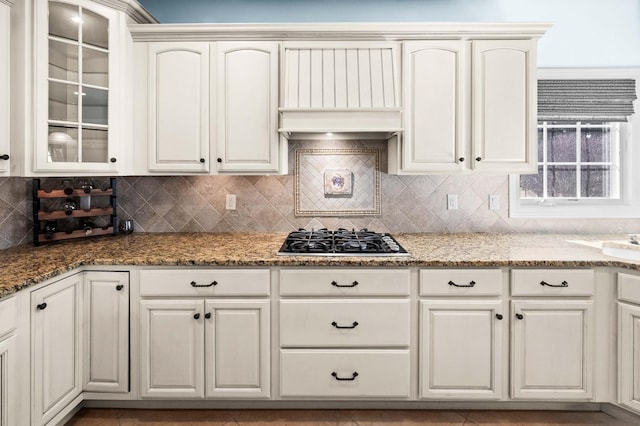 kitchen with glass insert cabinets, light stone countertops, gas stovetop, and tasteful backsplash