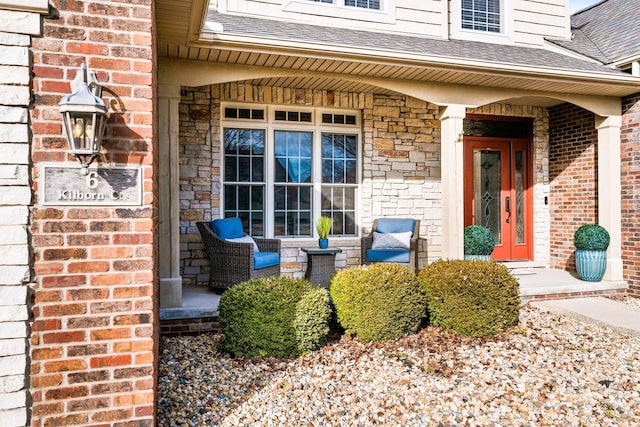 entrance to property with covered porch, brick siding, and roof with shingles