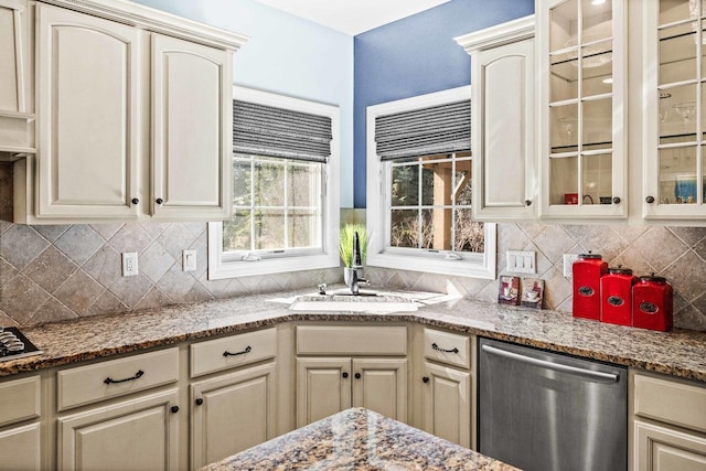 kitchen featuring backsplash, cream cabinets, glass insert cabinets, a sink, and dishwasher