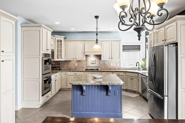 kitchen featuring stainless steel appliances, cream cabinets, glass insert cabinets, light tile patterned flooring, and a kitchen island