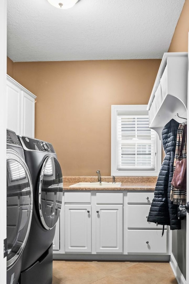 clothes washing area featuring cabinet space, light tile patterned floors, a textured ceiling, washing machine and dryer, and a sink