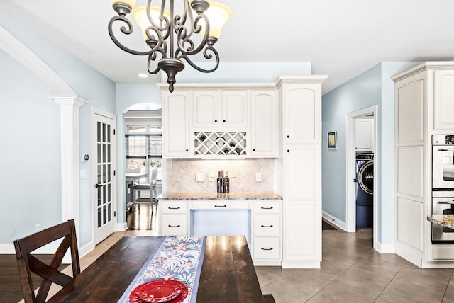 kitchen with arched walkways, tasteful backsplash, an inviting chandelier, light stone countertops, and washer / dryer