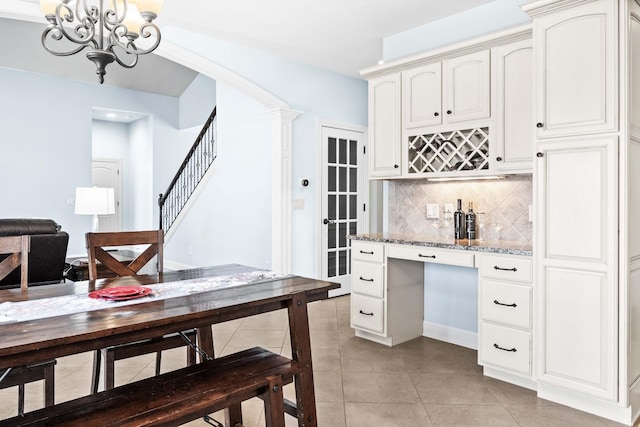 kitchen with light tile patterned floors, tasteful backsplash, a chandelier, light stone counters, and white cabinetry