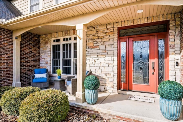 entrance to property with stone siding, a porch, roof with shingles, and brick siding