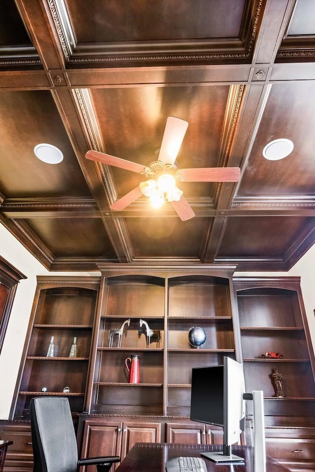 unfurnished office with coffered ceiling, built in features, a ceiling fan, and crown molding