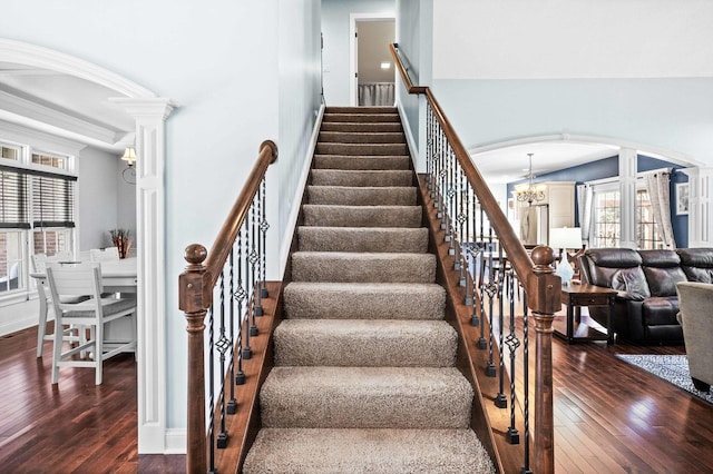 staircase featuring arched walkways, wood-type flooring, a notable chandelier, and decorative columns