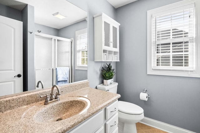 bathroom featuring toilet, a stall shower, baseboards, and vanity