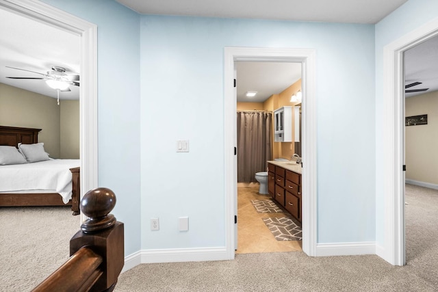 bedroom featuring baseboards, connected bathroom, and light colored carpet