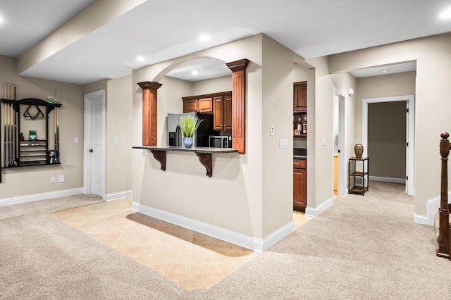 kitchen featuring decorative columns, baseboards, light colored carpet, stainless steel fridge with ice dispenser, and a kitchen bar