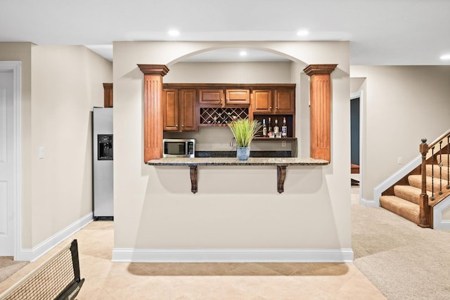 kitchen with stainless steel appliances, a kitchen bar, light stone countertops, and ornate columns