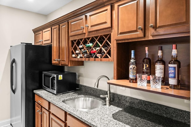 kitchen featuring brown cabinets, light stone countertops, stainless steel appliances, and a sink