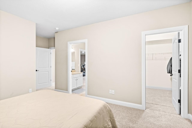 bedroom with a closet, light colored carpet, a spacious closet, ensuite bath, and baseboards