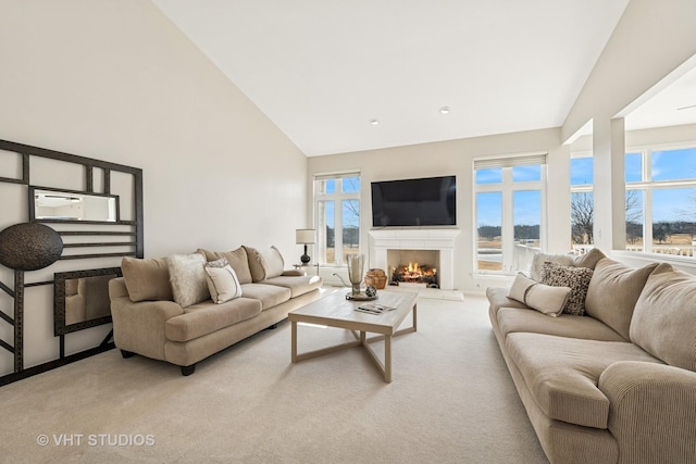 living area with high vaulted ceiling, light carpet, plenty of natural light, and a lit fireplace