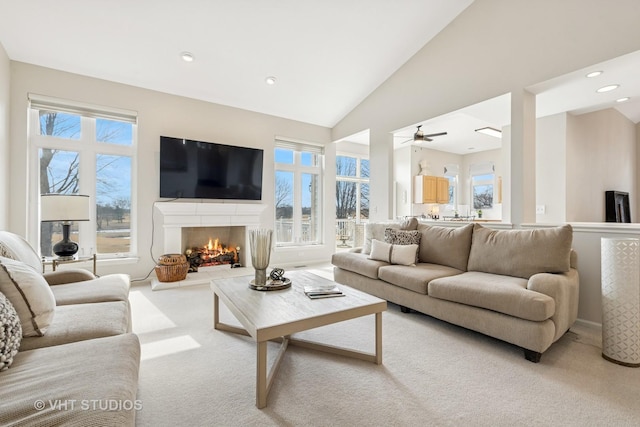 living area featuring a healthy amount of sunlight, a lit fireplace, high vaulted ceiling, and carpet flooring