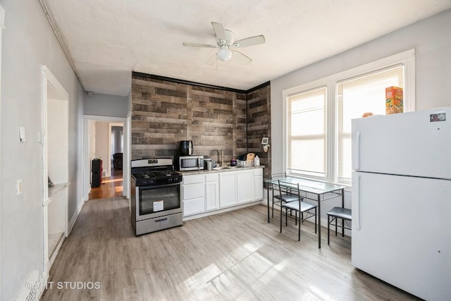 kitchen with stainless steel appliances, light wood-style flooring, white cabinets, wood walls, and ceiling fan