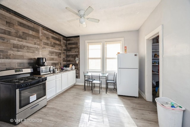 kitchen featuring light wood finished floors, wooden walls, ceiling fan, appliances with stainless steel finishes, and white cabinetry