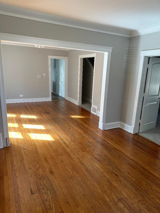 spare room featuring baseboards, visible vents, crown molding, and wood finished floors