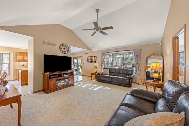 living area with light carpet, baseboards, visible vents, a ceiling fan, and high vaulted ceiling