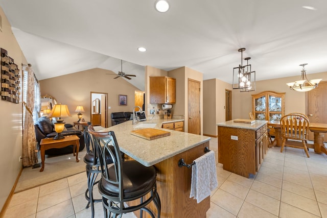 kitchen featuring brown cabinets, light tile patterned floors, vaulted ceiling, a sink, and a peninsula