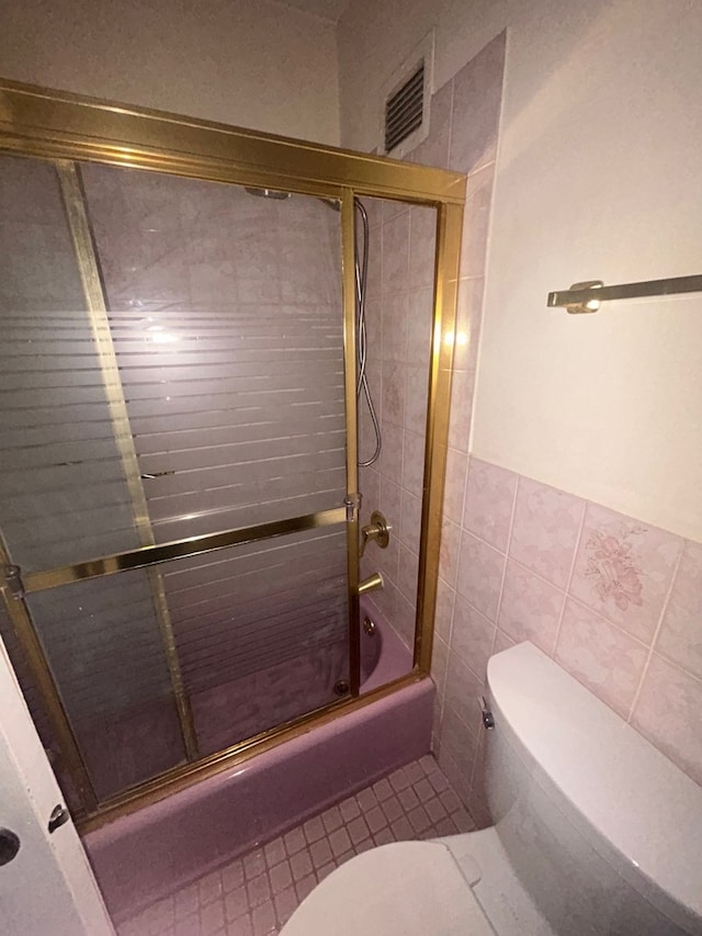 full bathroom featuring visible vents, bath / shower combo with glass door, toilet, tile patterned flooring, and tile walls