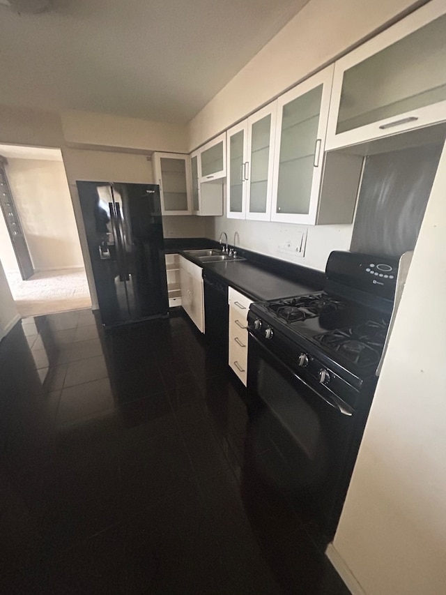 kitchen featuring dark countertops, glass insert cabinets, white cabinets, a sink, and black appliances