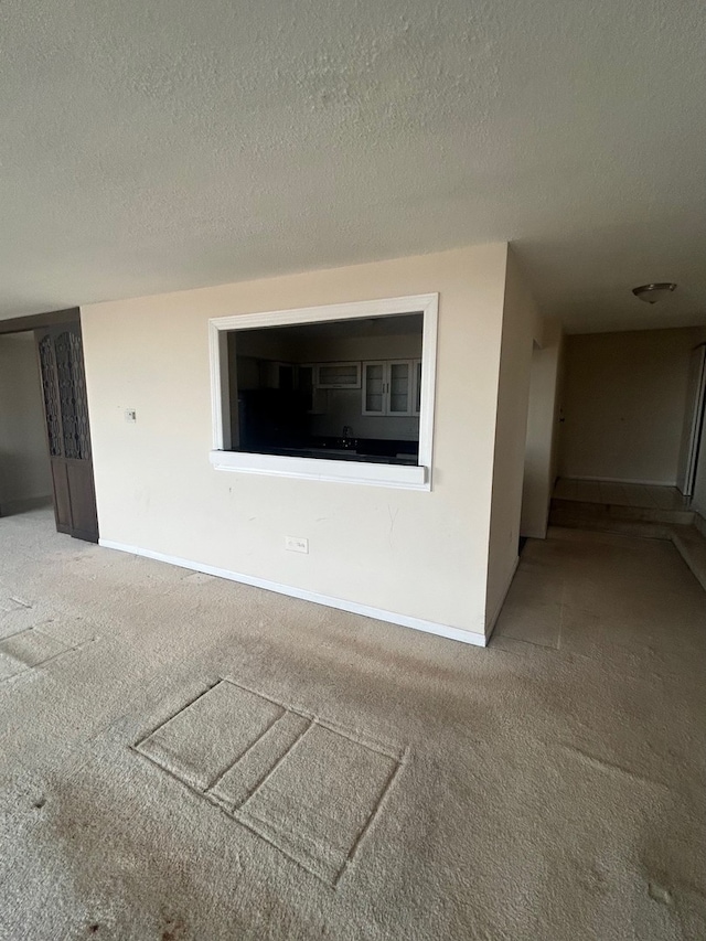 unfurnished living room featuring a textured ceiling, carpet flooring, and baseboards