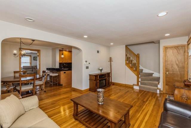 living area with arched walkways, recessed lighting, light wood-style flooring, baseboards, and stairs