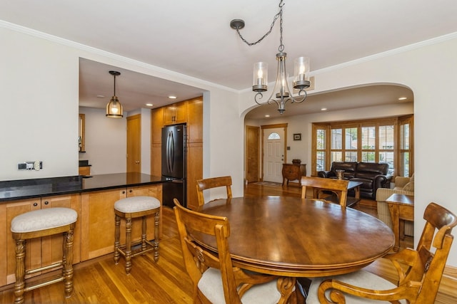 dining space with light wood finished floors, arched walkways, a chandelier, and crown molding