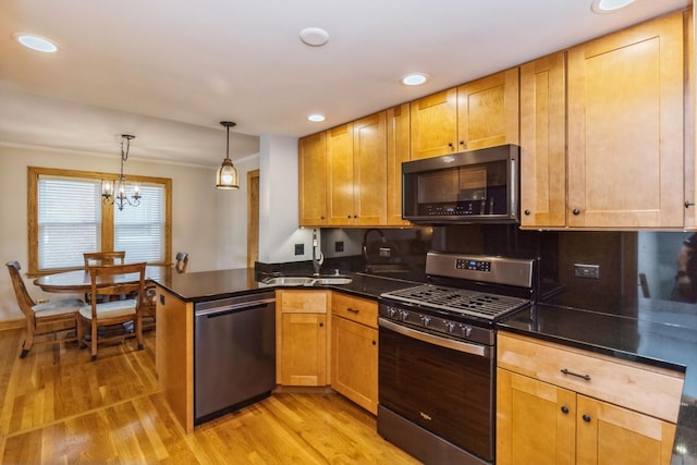 kitchen featuring a peninsula, light wood-style floors, hanging light fixtures, appliances with stainless steel finishes, and dark countertops